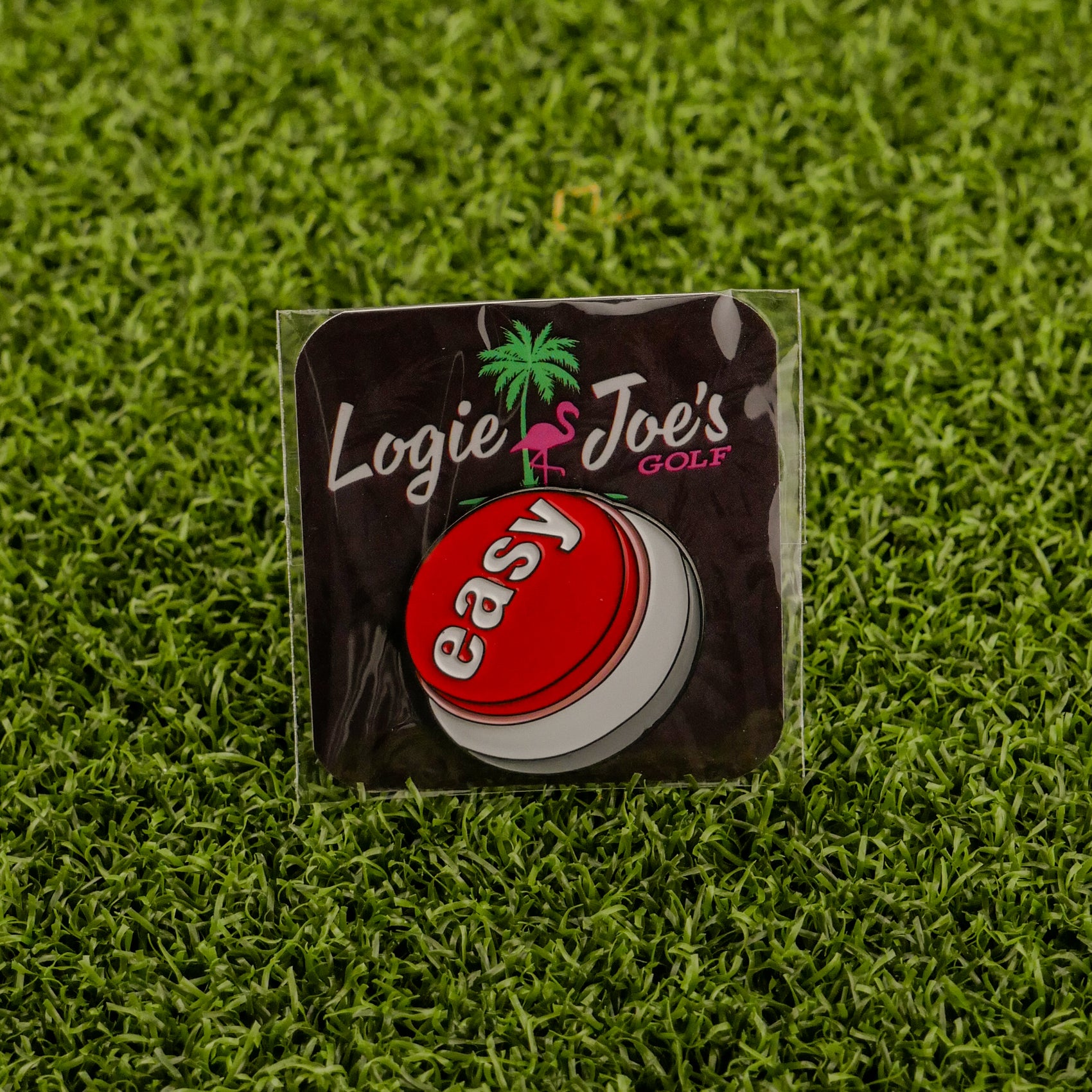 The Easy Button, a red and white golf ball marker labeled easy, is packaged on green turf with the Ballmarkers by Logie Joes brand and palm tree logo. Add style to your game with Ballmarkers by Logie Joes.