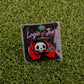 A premium Eat Sh*t & Die ball marker pin by Ballmarkers by Logie Joes, featuring a cartoon grim reaper with a golf club and Logie Joe’s Golf in white and pink, displayed on artificial green grass.
