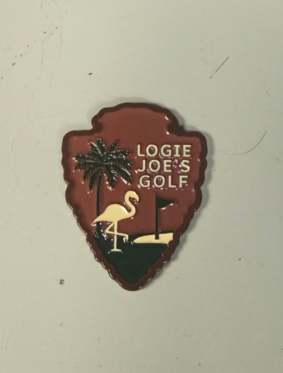 Introducing the National Park Ball Marker by Logie Joe's Golf—a shield-shaped pin uniquely crafted with a palm tree, flamingo, and golf hole, set against a brown background inspired by national park signs and featuring the Logie Joe's Golf logo.