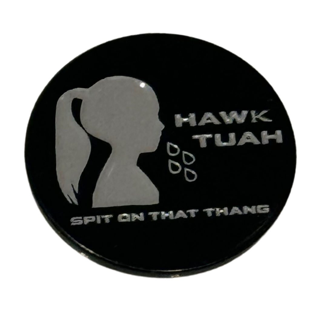 The Hawk Tuah 💦 Ball Marker by TeeBumps is a round black marker with a silver woman’s profile spitting, ponytail visible, "HAWK TUAH" above and "SPIT ON THAT THANG" below, plus four illustrated spit droplets.