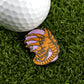 A golf ball rests on artificial grass beside the Face Hugger by Ballmarkers.com—a premium ball marker shaped like an alien embracing a human face with "Free Hugs" inscribed, making it a truly unique golf accessory.