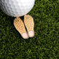 A golf ball rests on artificial grass next to the Logie Joe's Golf Feet Ball Marker, a fun golfer accessory shaped like cartoonish, hairy bare feet.
