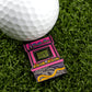 A Logie Joe's Golf ball with a premium marker sits on artificial grass next to a Florida Man (Game Over) arcade pin, featuring "GAME OVER" on the screen.