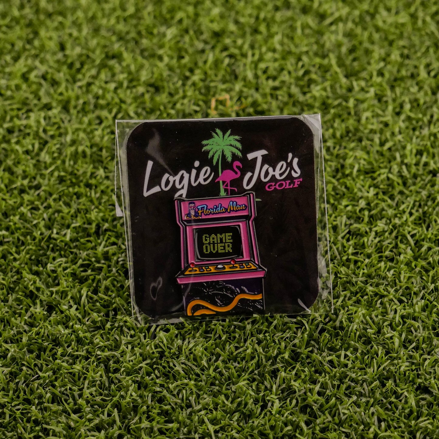 The Florida Man (Game Over) enamel pin by Logie Joe's Golf features an arcade machine with Florida Man, Game Over text, a flamingo, and palm tree on artificial grass—a funny golf accessory that doubles as a unique ball marker.