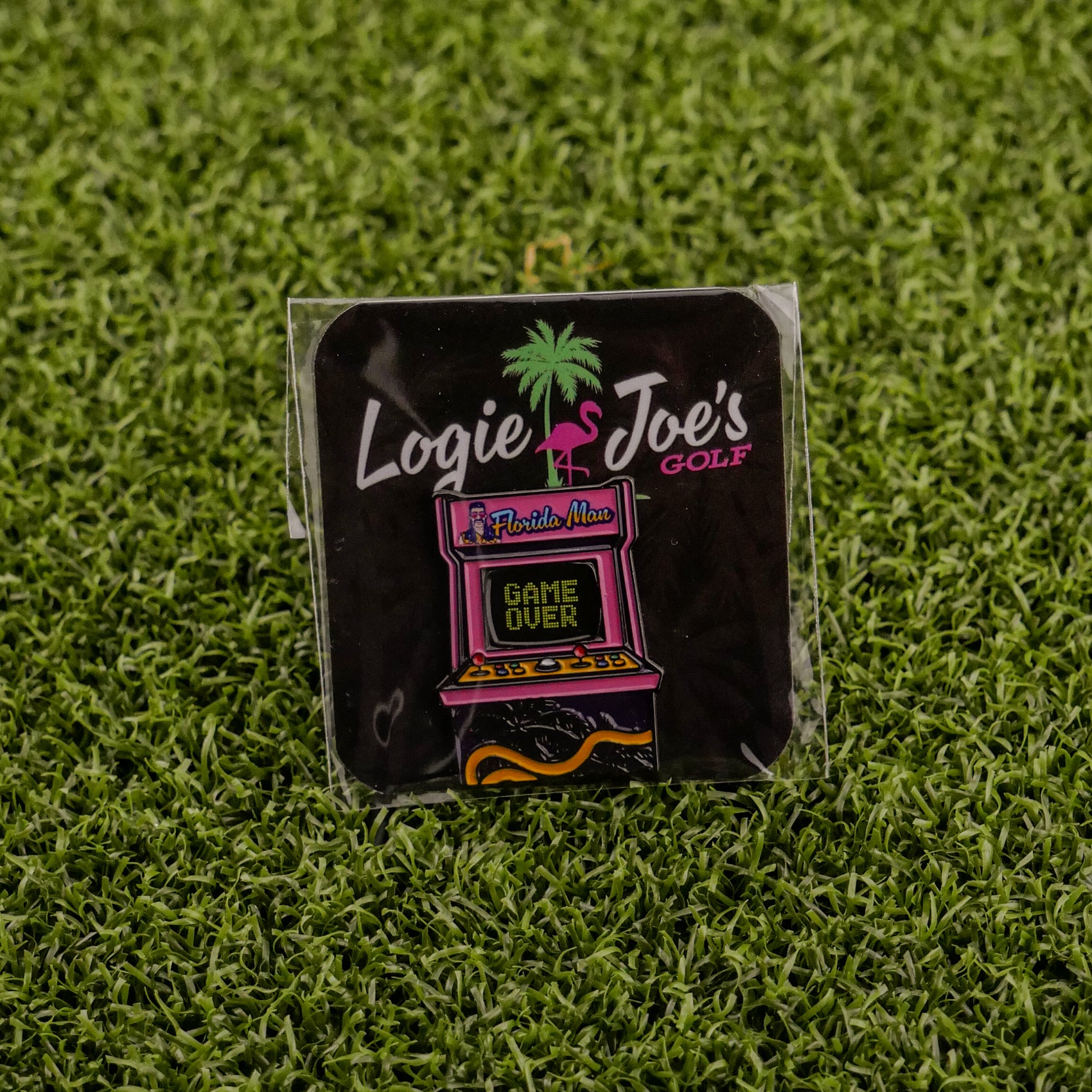 The Florida Man (Game Over) enamel pin by Logie Joe's Golf features an arcade machine with Florida Man, Game Over text, a flamingo, and palm tree on artificial grass—a funny golf accessory that doubles as a unique ball marker.