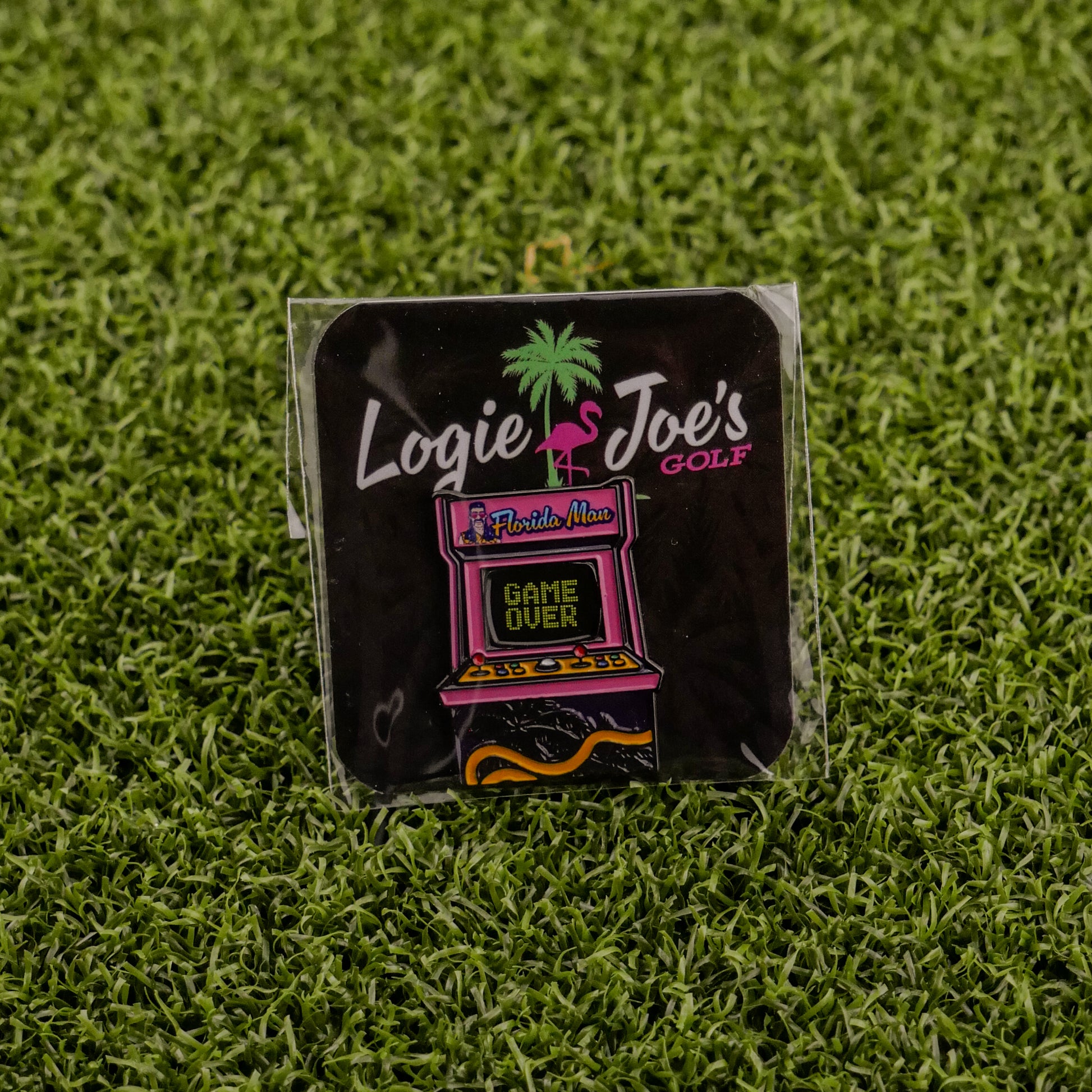 The Florida Man (Game Over) enamel pin by Logie Joe's Golf features an arcade machine with Florida Man, Game Over text, a flamingo, and palm tree on artificial grass—a funny golf accessory that doubles as a unique ball marker.