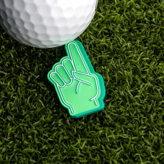 A Foam Finger #1 Ball Marker by Ballmarkers.com and a golf ball rest on artificial green grass, the foam finger pointing upward in celebration.