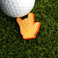 A golf ball sits on artificial grass beside the Ballmarkers.com Foam Finger Rock On Ball Marker, shaped like a hand making the rock on gesture with vibrant orange and yellow accents.