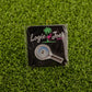 The Logie Joe's Golf "Magnify Glass" pin features a magnifying glass design with "putter" inside, set on green turf—a unique golf ball marker and a funny accessory for your collection.