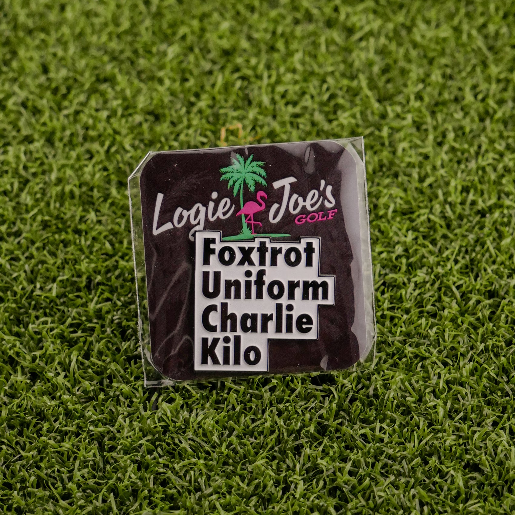 A premium ball marker from Logie Joe's Golf, featuring a palm tree logo and the phrase "Foxtrot Uniform Charlie Kilo" in bold black letters—a humorous addition to any golfer’s collection.