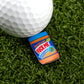 A miniature jar of Ballmarkers.com Chunky Peanut Butter labeled "F*CK ME SUPER CHUNK" rests beside a golf ball and premium golf accessories on artificial green grass.