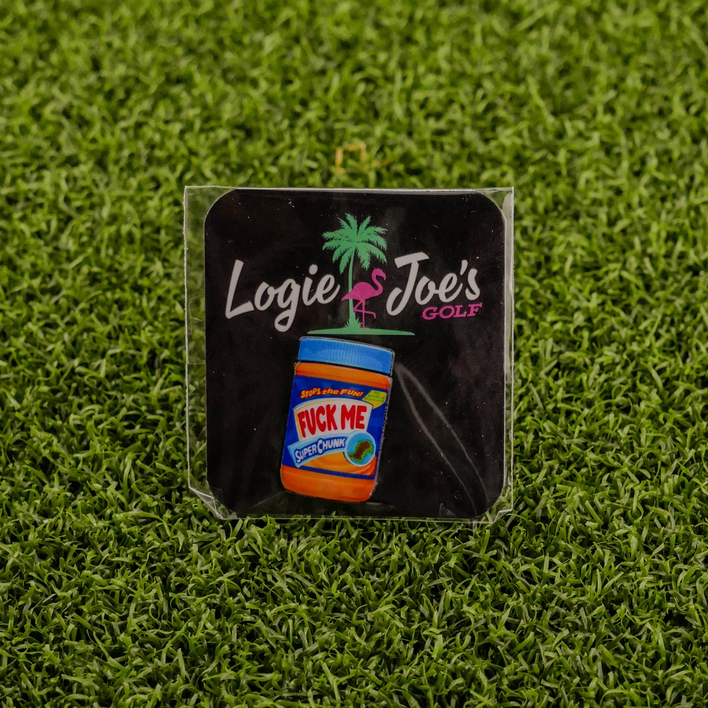 A square sticker on green turf featuring Ballmarkers by Logie Joes Chunky Peanut Butter text, a pink flamingo, palm tree, and a peanut butter jar—ideal for fans of novelty and golf ball markers.