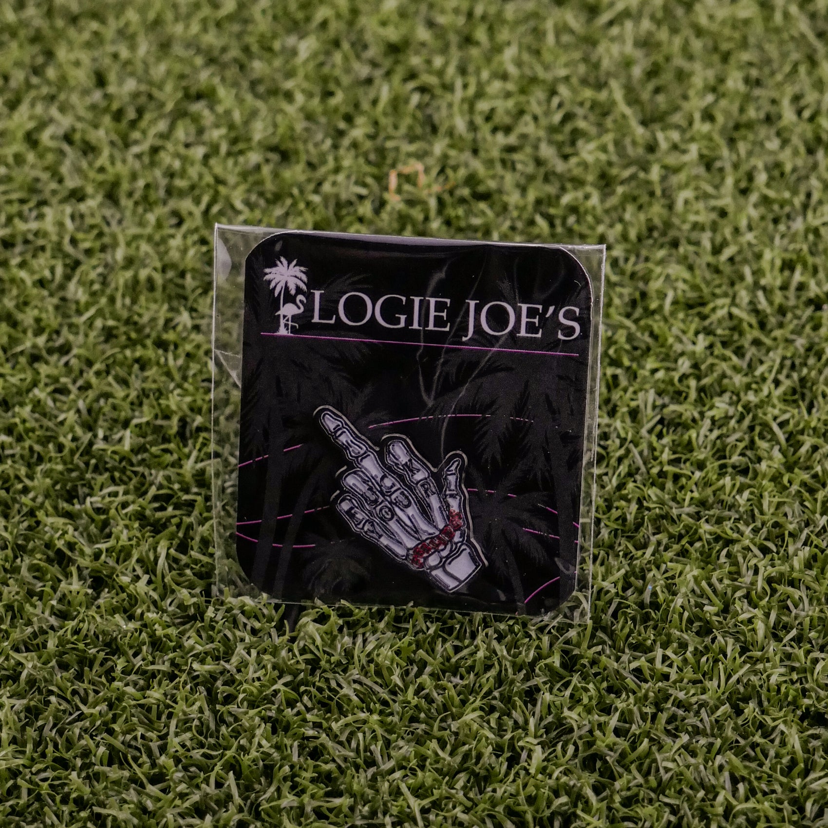 The “F” Your Feelings pin from Logie Joe's Golf, featuring a skeleton hand gesture, is displayed on branded card atop artificial grass—a standout golf ball marker or unique gift for fans of bold golf accessories.
