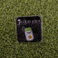 The Jar of “F”s enamel pin by Ballmarkers by Logie Joes sits on a branded card atop artificial grass—perfect as a funny ball marker or gift for fans of unique golf accessories.