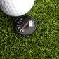 A golf ball rests on artificial grass beside the Ballmarkers.com Empty Tank Ball Marker, shaped like a car fuel gauge, reminding golfers to "refuel" during their game.