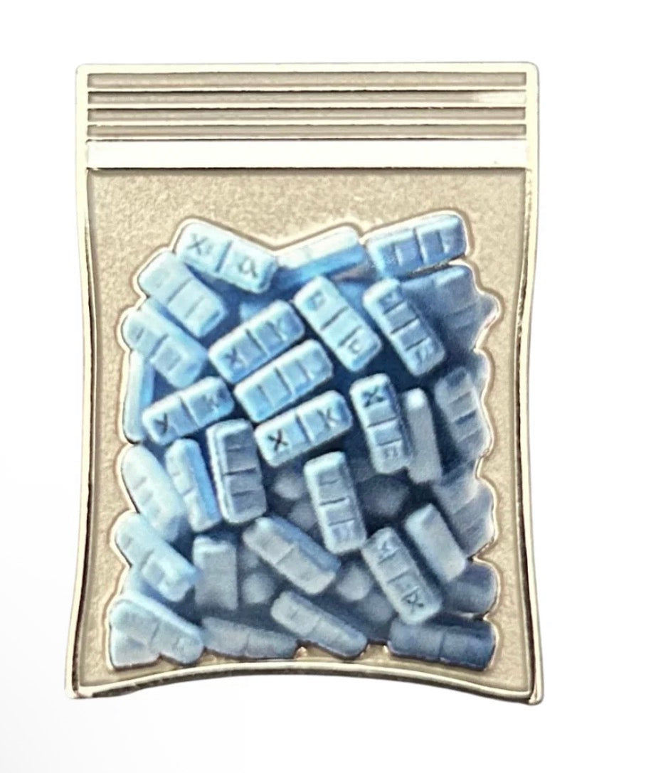 Introducing the Xanny Bars Ground Score Ball Marker by Tee Bumps: a pin crafted in the shape of a small plastic bag filled with blue rectangular pills, each stamped with “XANAX.” Featuring a silver border and ziplock-style top, this unique accessory is ideal for collectors or as a standout golf ball marker—perfect for those who love the Bars Ground Score aesthetic.
