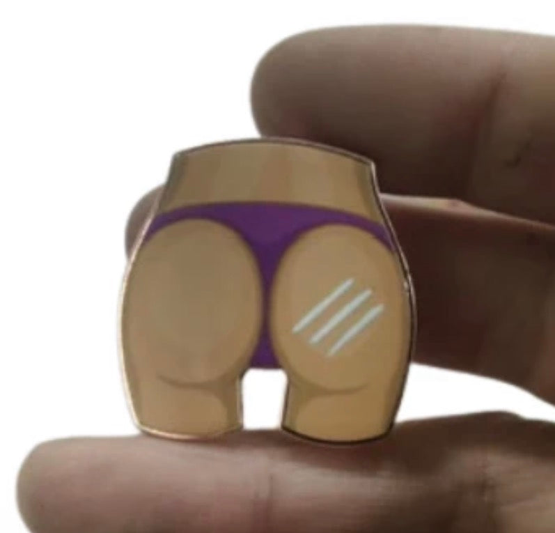 A person holds Tee Bumps’ Rack on the Back Ball Marker—shaped like the lower half of a body in purple underwear, with cartoon-style skin and a white line detail—cleverly designed for golf enthusiasts.