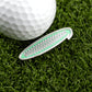 A white golf ball and Logie Joe's Golf Gooooooooooo! Speech Bubble marker in green with silver lettering rest on artificial grass—ideal for fans of unique, personalized golf accessories.