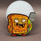 The Gill Cheese Ball Marker by Crown Golf Designs features a cartoonishly angry grilled cheese character with a metal spatula, standing before a giant golf ball, with melted cheese dripping and a fierce look.