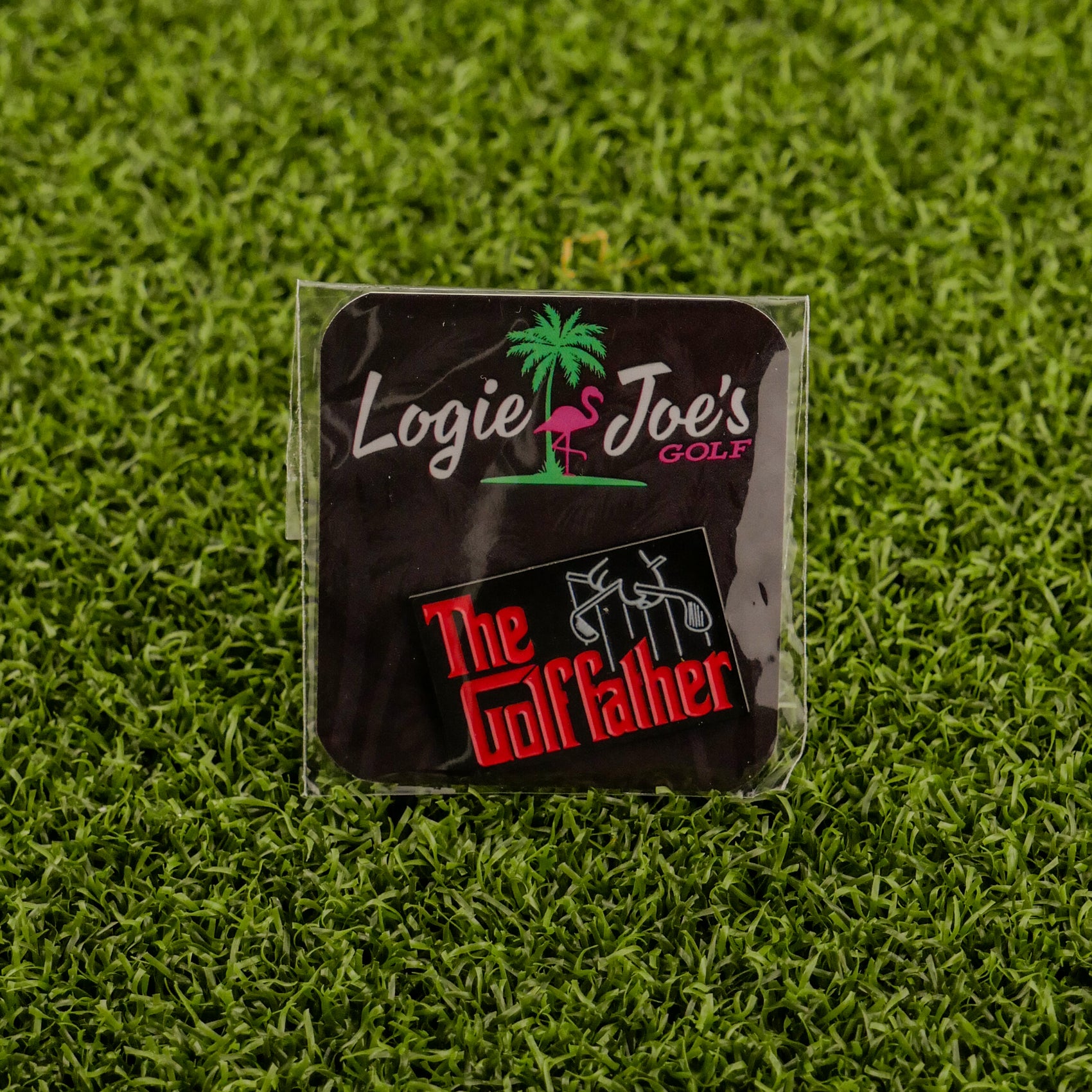 A square black Logie Joe's Golf sticker with a pink flamingo sits above another labeled "The Golf Father" in red and white on green turf—a funny, quirky golf accessory or golf ball marker for your bag.