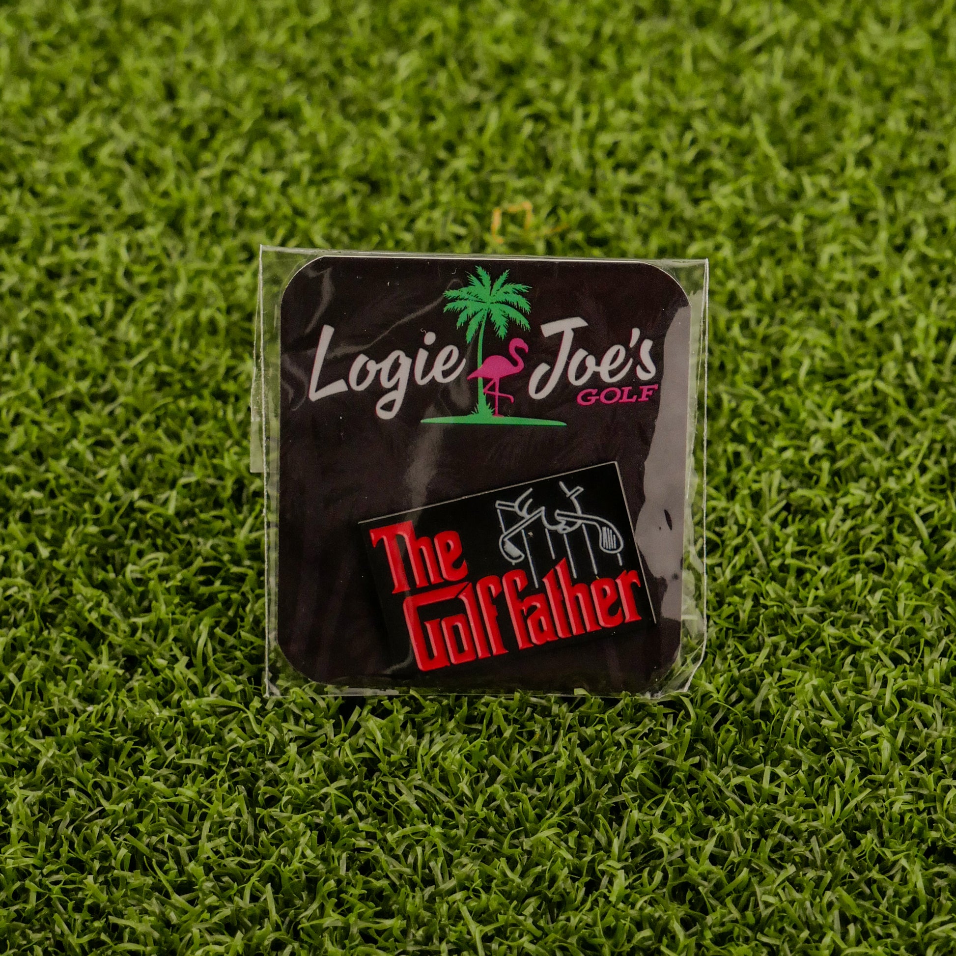 A square black Logie Joe's Golf sticker with a pink flamingo sits above another labeled "The Golf Father" in red and white on green turf—a funny, quirky golf accessory or golf ball marker for your bag.