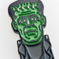 A close-up of the Frankenstein Ball Marker by Pins and Aces, a fun magnetic golf accessory shaped like Frankenstein’s monster with a green face, bolts in the head, and a black suit for golf enthusiasts.