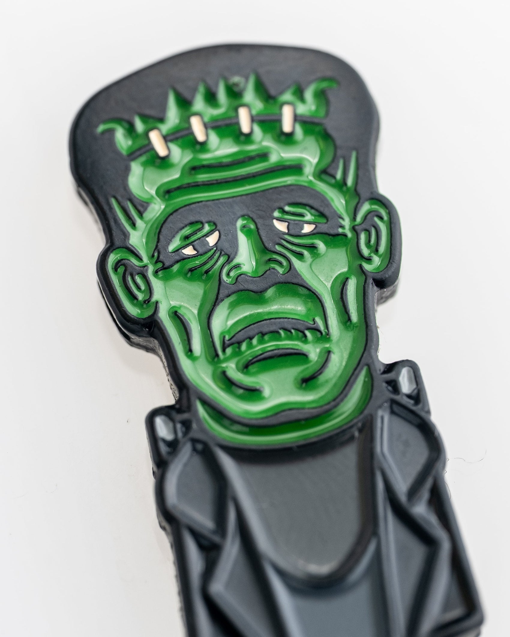 A close-up of the Frankenstein Ball Marker by Pins and Aces, a fun magnetic golf accessory shaped like Frankenstein’s monster with a green face, bolts in the head, and a black suit for golf enthusiasts.
