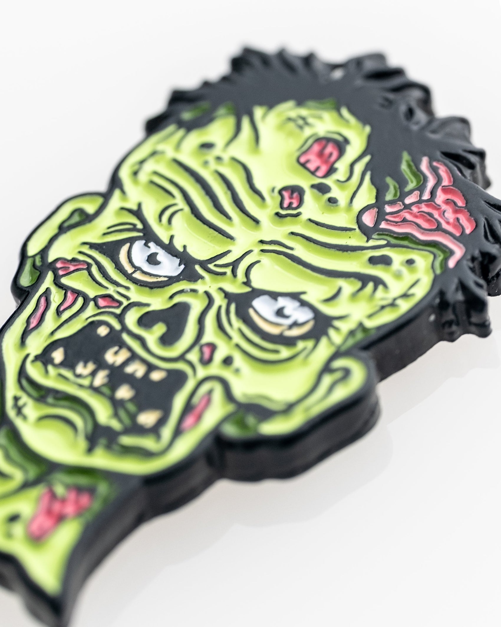 A close-up of the Mutant Zombie - Ball Marker by Pins and Aces, featuring a vibrant cartoon zombie head with green skin and angry eyes, designed as a colorful magnetic golf accessory for collectors, shown on a white background.