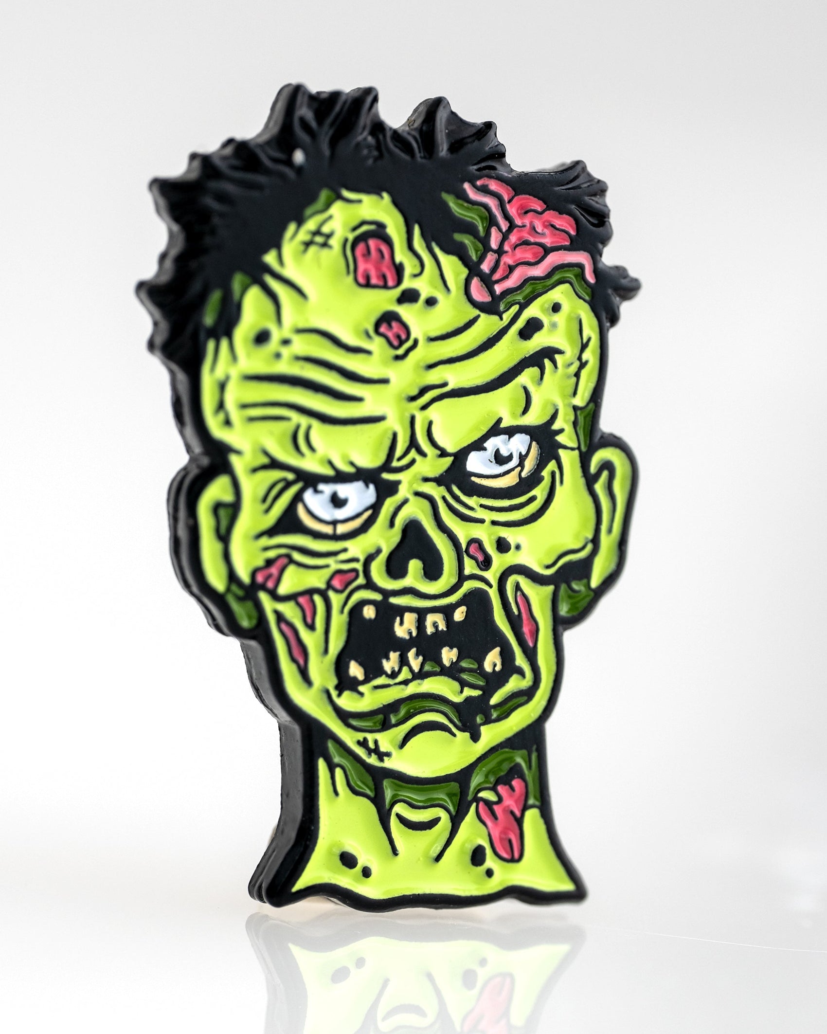 The Mutant Zombie - Ball Marker by Pins and Aces features a cartoonish green zombie head with exposed brains, black messy hair, and an angry look, displayed on a plain white background.