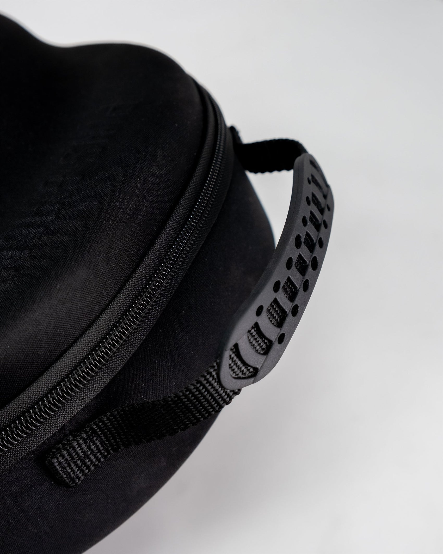Close-up of the Pins and Aces Hat Caddie, a black zippered golf hat case featuring a textured plastic handle and fabric strap, shown against a plain white background.