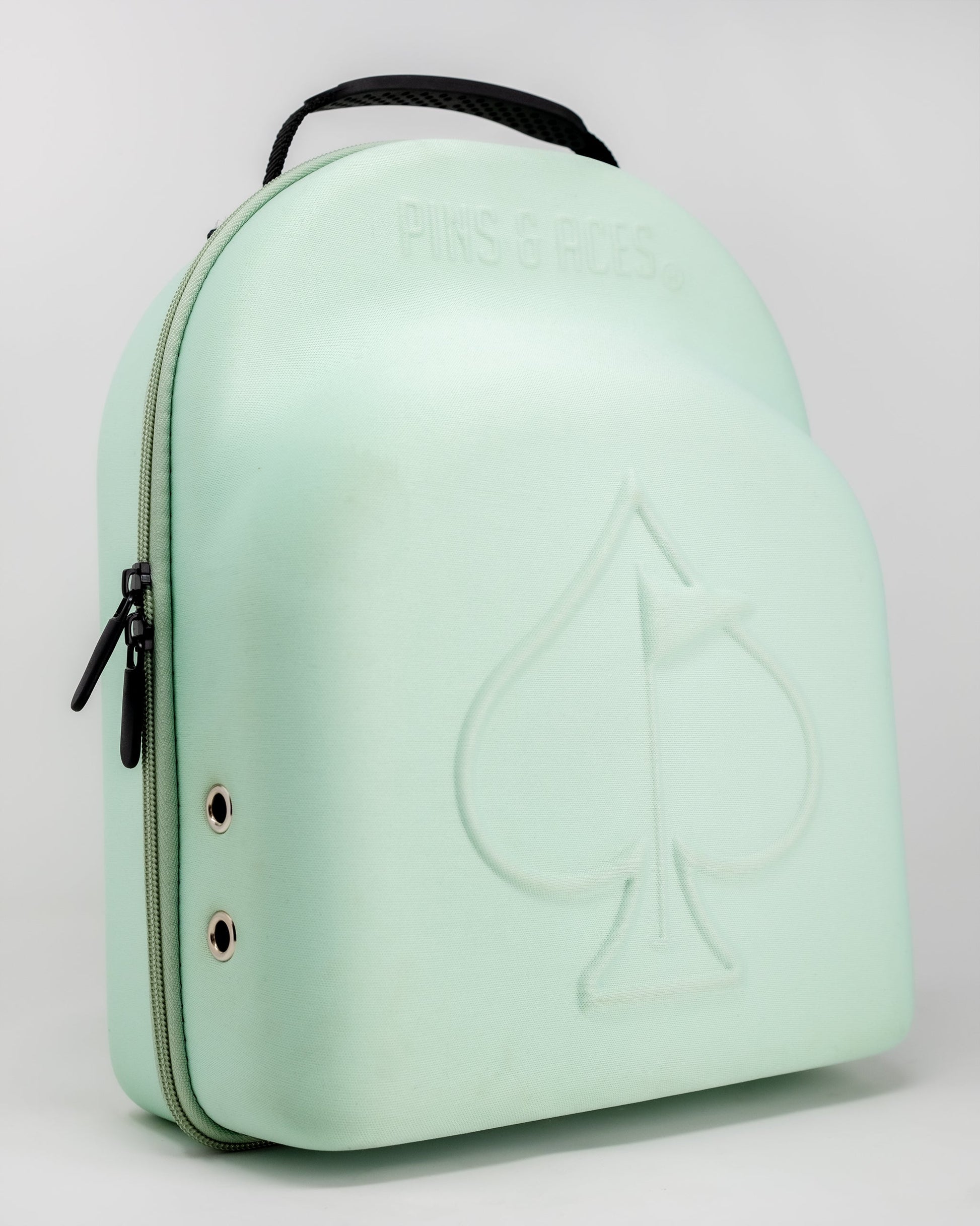 The Pins and Aces Hat Caddie is a light green hat case with handle, zipper closure, and two grommet holes. An embossed spade with flag and "PINS & ACES" decorates the front—perfect for carrying hats on or off the course.