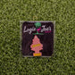 A pink tree-shaped air freshener labeled “Hitten Trees Life’s a Peach” by Logie Joe’s Golf sits on artificial green grass, bringing a playful vibe to funny golf accessories.