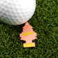 A white golf ball rests on green turf beside Logie Joe's Golf Hitten Trees Life’s a Peach, a peach-colored tree-shaped air freshener—ideal for fans of funny golf accessories and unique golf ball markers.