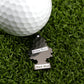 A white golf ball rests on green artificial grass beside a tree-shaped black tag labeled "Hitten Trees" and "Black Slice"—a fun accessory from Logie Joe's Golf to add personality to your game.