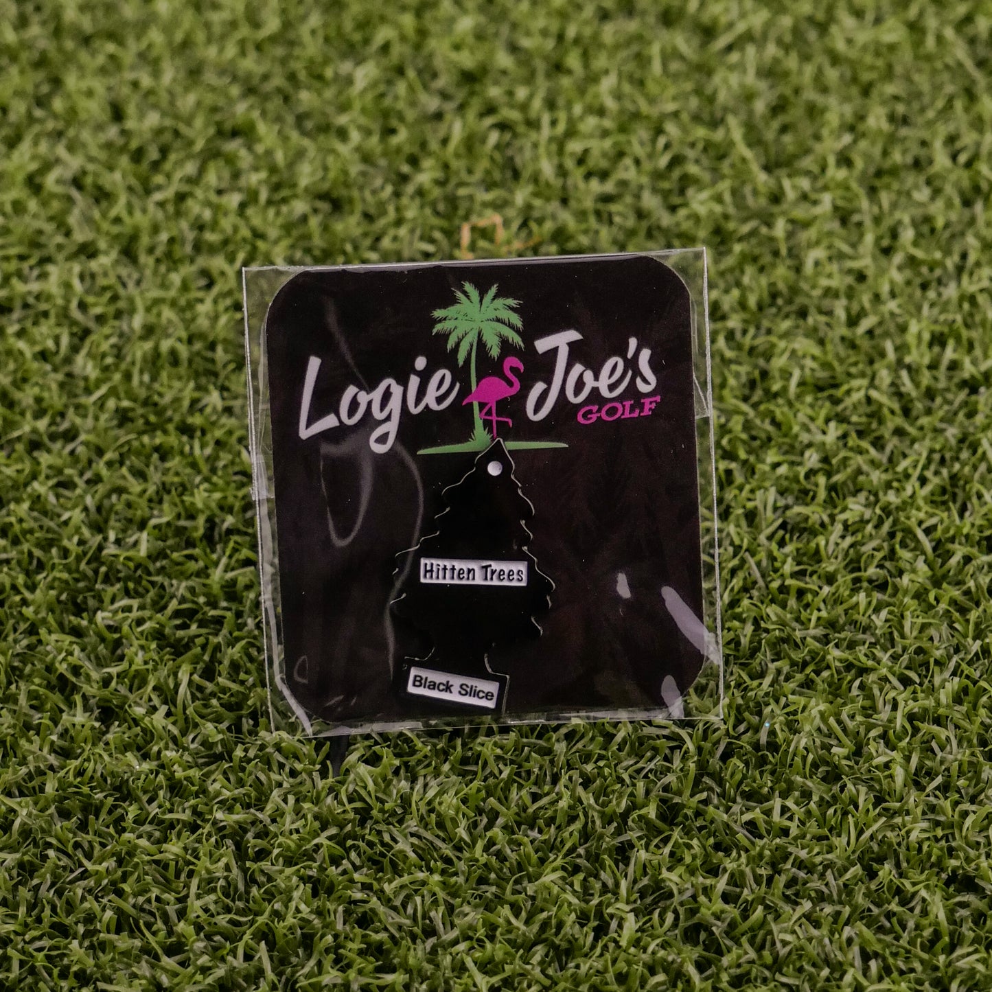 The Logie Joe's Golf Hitten Trees Black Slice air freshener comes packaged on artificial grass with a palm tree and flamingo logo—ideal for golf fans looking for funny accessories or unique gifts.