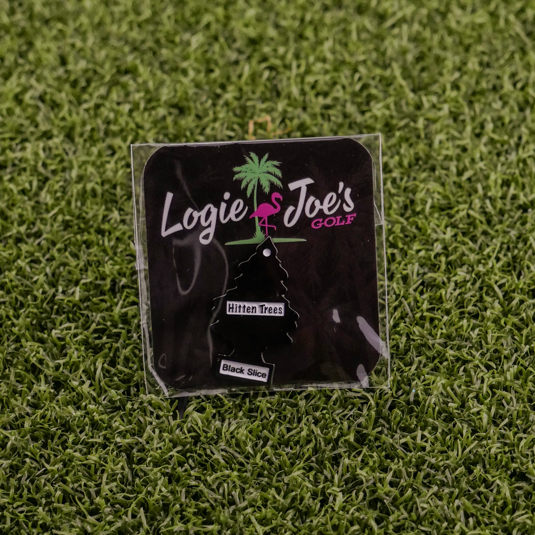 The Logie Joe's Golf Hitten Trees Black Slice air freshener comes packaged on artificial grass with a palm tree and flamingo logo—ideal for golf fans looking for funny accessories or unique gifts.