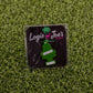 A green, tree-shaped ball marker labeled Hitten Trees NutNBut Trees by Ballmarkers from Logie Joes is attached to a black card with brand text—an amusing gift idea for golf lovers, displayed on artificial grass.