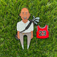 The GOAT 23 enamel pin by Pin Creatures features a smiling bald man in golf gear with clubs, standing on grass next to a red #23 jersey—an ideal golf accessory or unique ball marker for any fan.