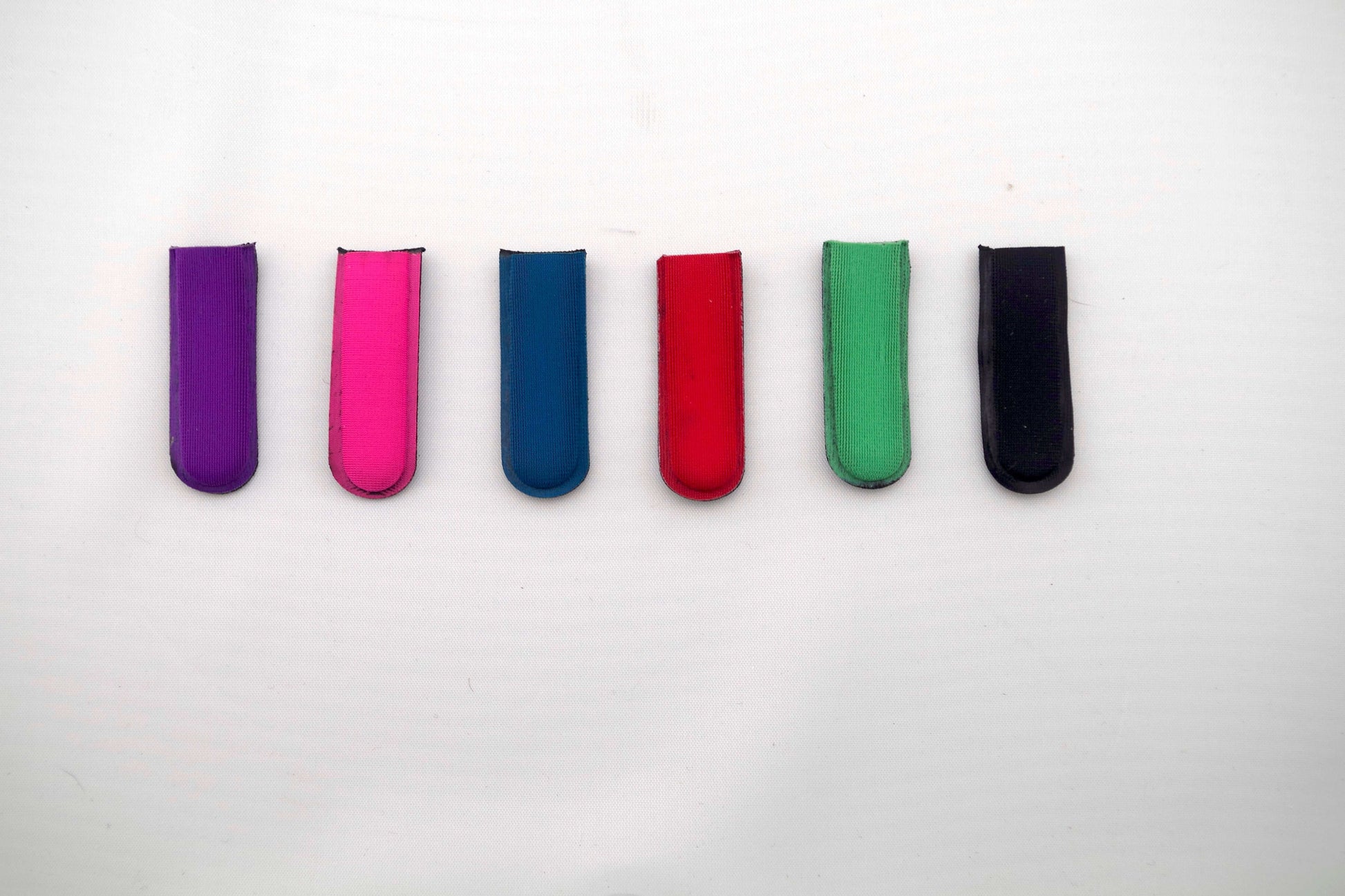 Six THE BYRD GOLF DIVOT CLYPs by The Byrd, LLC in purple, pink, blue, red, green, and black are lined up horizontally on a white background. HOT PRODUCT—organize your golf gear now while supplies last!.