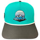 Introducing the Mountain Moonrise Golf Hat by Logie Joe’s Golf—a turquoise and gray snapback cap featuring a mountain and sun graphic on the front panel. This outdoor golf hat offers white trim above the brim, a flat dark gray bill, and an adjustable snapback for comfort. Plus, it includes a built-in magnetic ball marker holder with marker included, making it perfect for any adventure on or off the course.