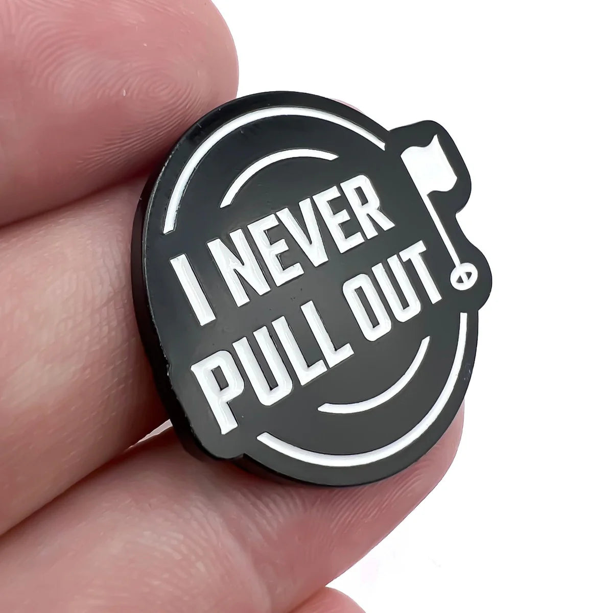 A hand holds the Bogey Bros "I Never Pull Out" round black pin with white text and a small golf flag icon, referencing the golf trend of leaving the flag stick in while putting.