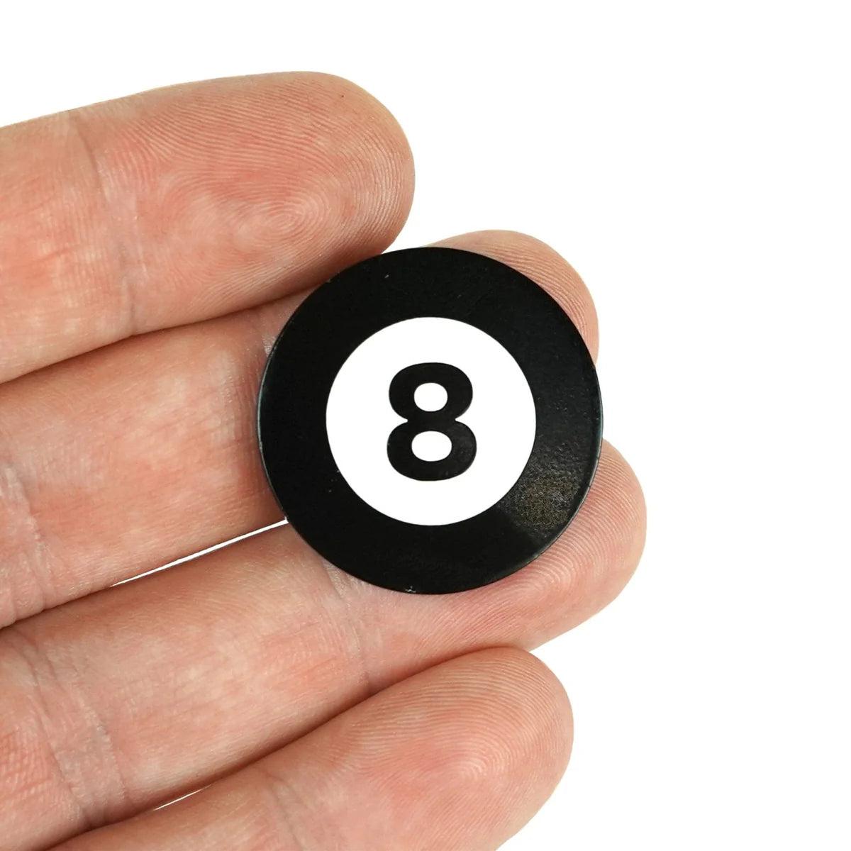 A close-up of a hand holding a small, round Magic 8 Ball token by Bogey Bros, featuring a black finish, white circle, and the number 8 in the center—designed as a miniature novelty gift.