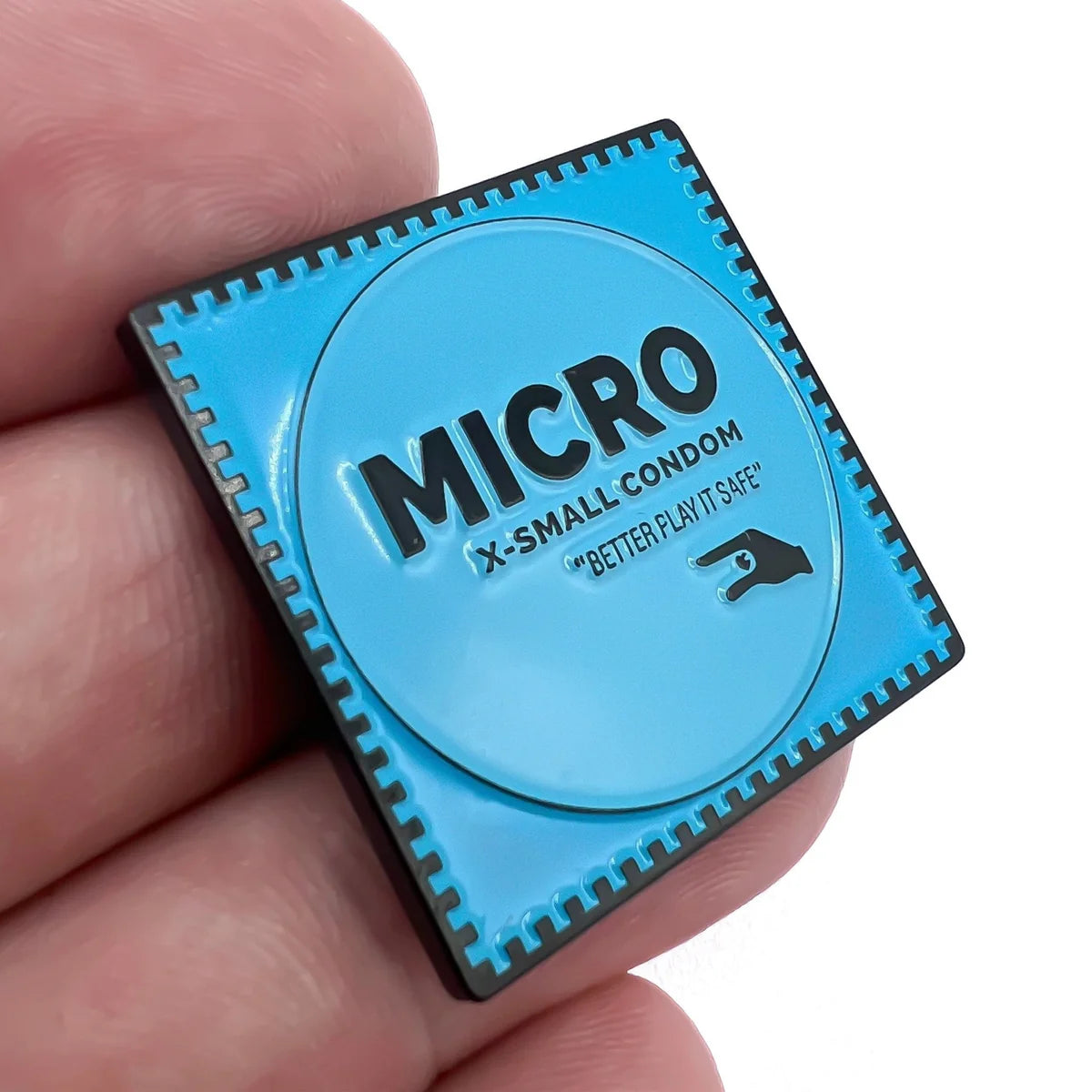 A hand holds a square blue pin that looks like a condom wrapper—a quirky golf ball marker from Bogey Bros called "Micro," featuring the text MICRO X-SMALL CONDOM BETTER PLAY IT SAFE and a small pointing hand graphic.