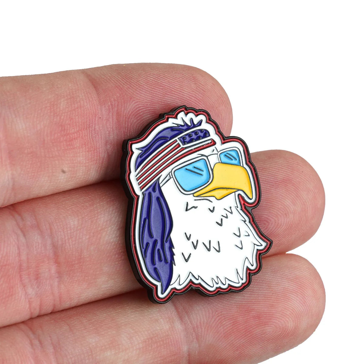 A hand holds the Bogey Bros FREEagle enamel pin, featuring an American Eagle wearing blue sunglasses and a red, white, and blue headband.