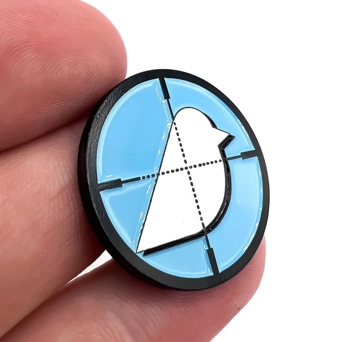 A hand holds the Birdie Hunter pin by Bogey Bros—featuring a simplified white bird on a light blue background with black crosshairs and a dashed center line, inspiring new possibilities.