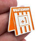 A close-up of a hand holding the Bogey Bros WHATABOGEY pin, shaped like a Whataburger table tent with "+1" in the center—perfect for marking that tough bogey after missing a long putt on the golf course.