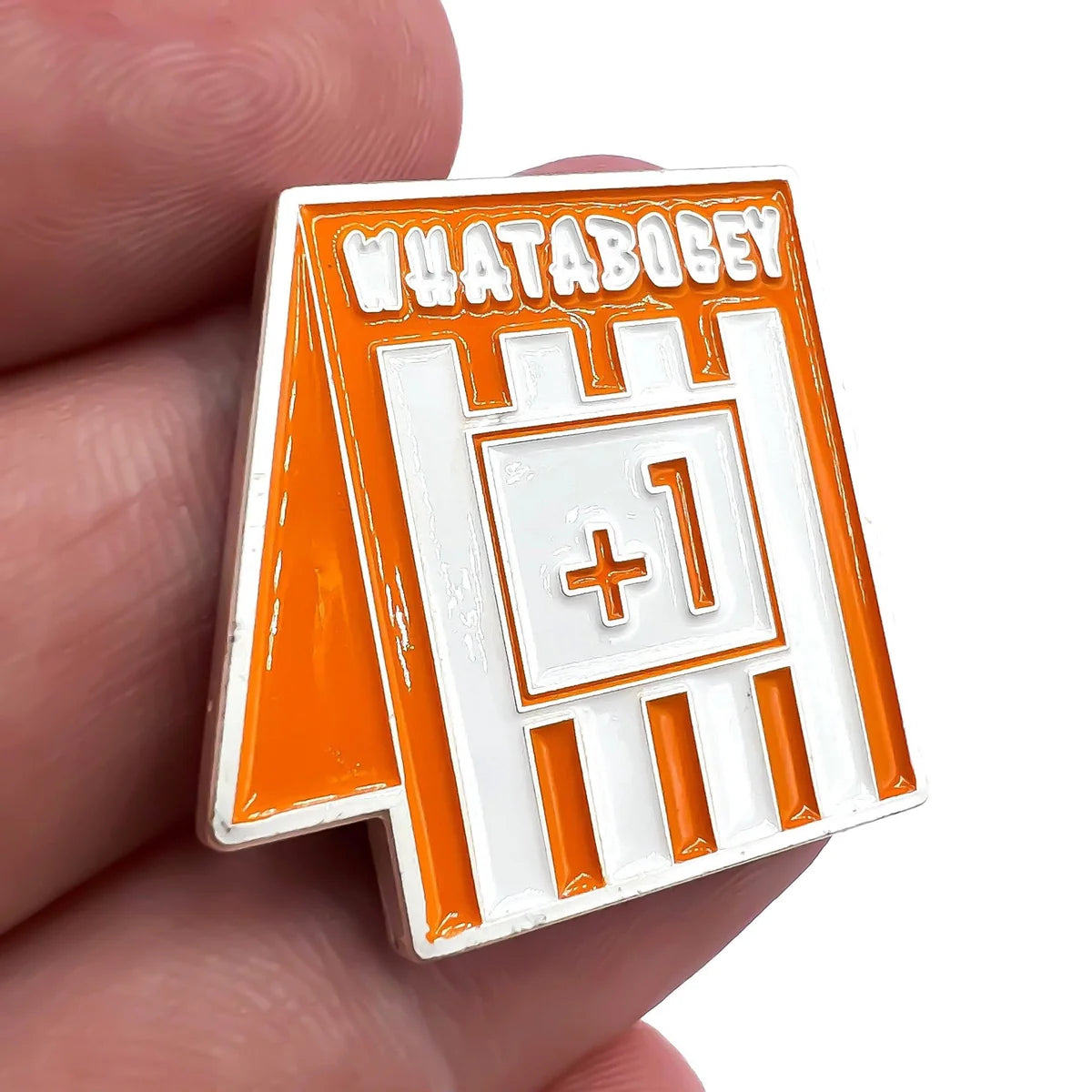 A close-up of a hand holding the Bogey Bros WHATABOGEY pin, shaped like a Whataburger table tent with "+1" in the center—perfect for marking that tough bogey after missing a long putt on the golf course.
