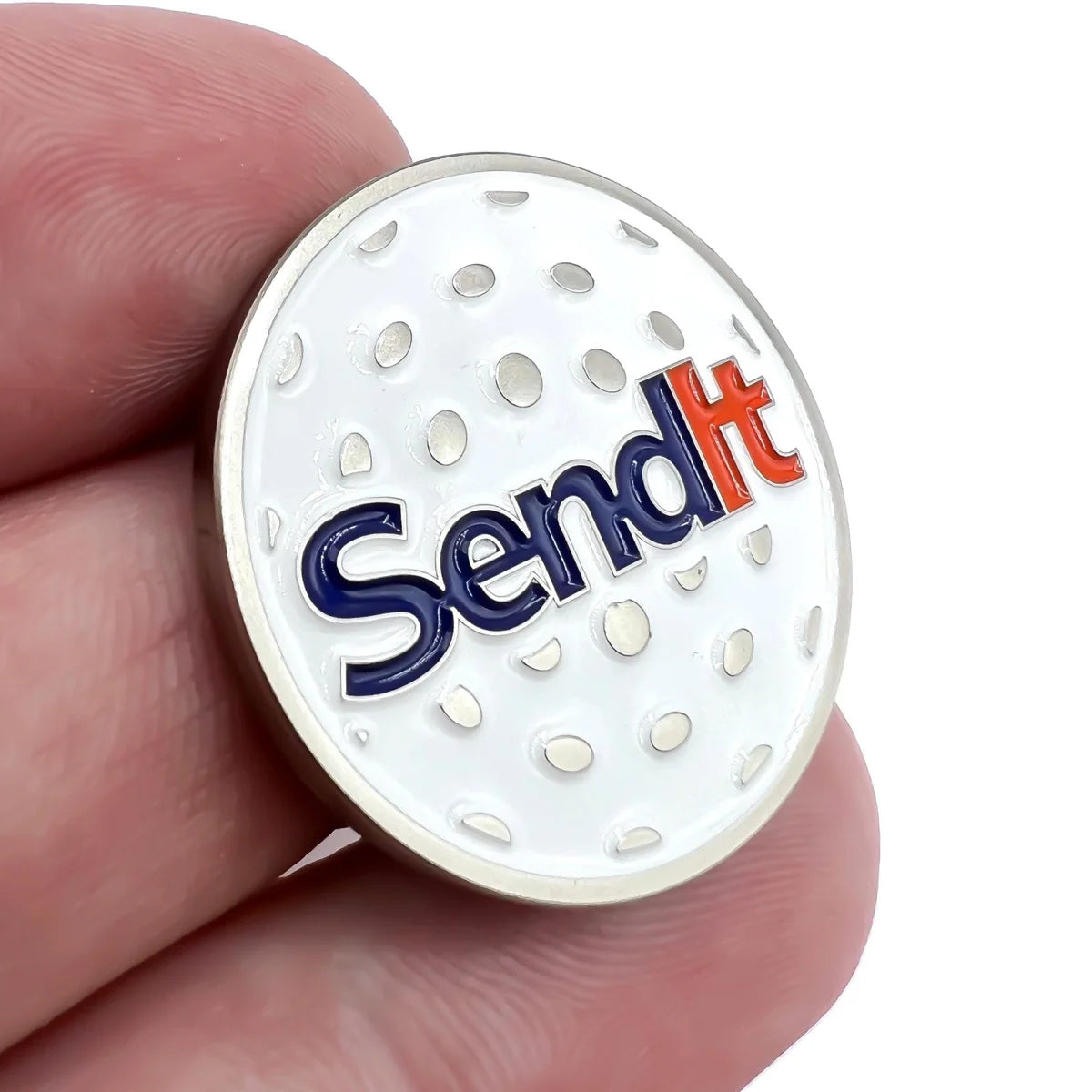 A hand holds the Bogey Bros "Send It" golf ball marker—a white, dimpled, circular accessory with bold blue and red letters—perfect for golfers eager to send it on the green.