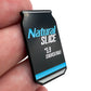 A golfer's hand holds a black Bogey Bros Natural Slice ball marker shaped like a can, displaying blue and white text saying "Natural SLICE *5.9 STROKES/HOLE" and featuring a bold blue stripe near the bottom.