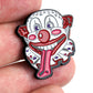 A close-up of the Bogey Bros "Happy Land Clown" enamel pin held between fingers, with a wide open mouth, long red tongue, red nose, and bold features—this could be Happy's nemesis in pin form.